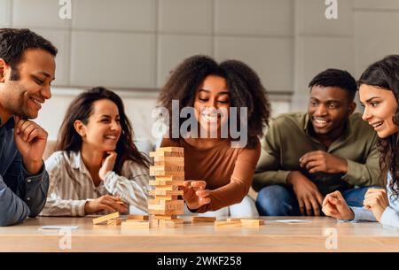 students group around table in kitchen engaging in board game Stock Photo