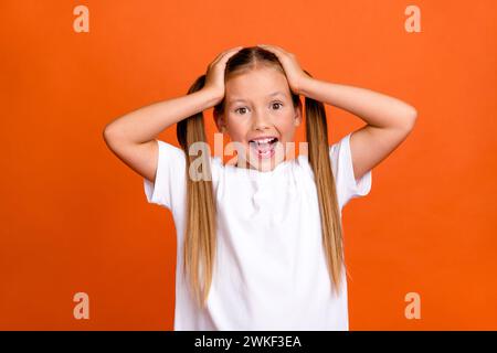 Photo portrait of charming little girl touch head shocked shout dressed stylish white clothes isolated on orange color background Stock Photo