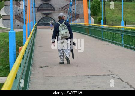 In the picture, a fisherman with a backpack on his back and fishing rods in his hand is walking across the bridge. Stock Photo