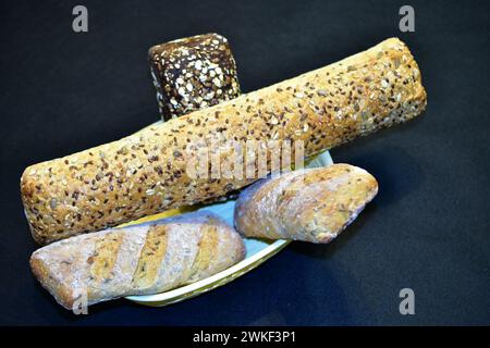 Baguettes of different lengths lie in a basket on a dark table. Stock Photo