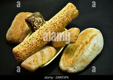 Baguettes of various lengths are in a basket, and on a dark table is a bun with a cracked top surface. Stock Photo