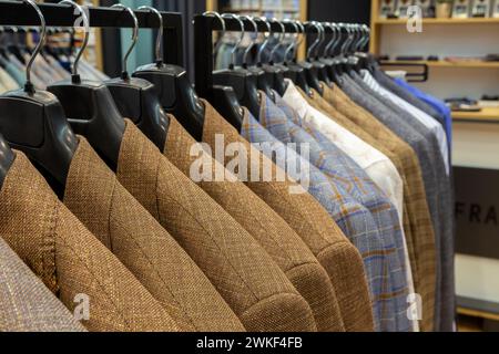 A row of men's suits, jackets hanging on a rack for display. Elegant man suit jackets hanging in a row on hangers. Stock Photo