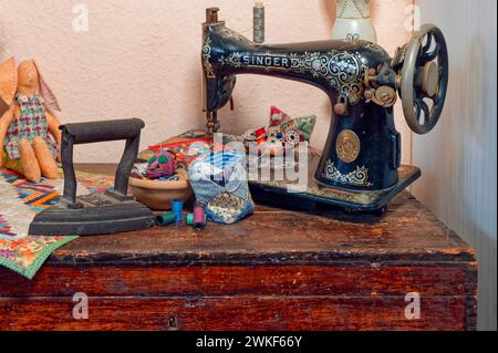 Berlin, Germany - January 16, 2024: Wooden chest on which a historical sewing machine and a historical iron stand amidst sewing utensils. Stock Photo