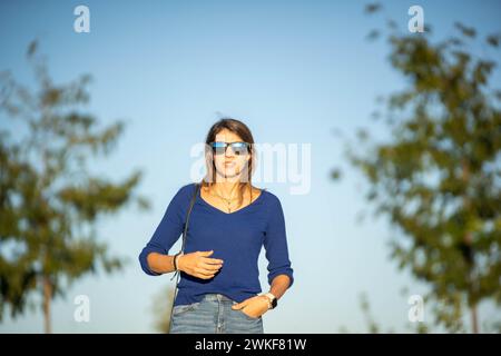 Front view of a relaxed woman with sunglasses walking outdoors at daytime. Stock Photo