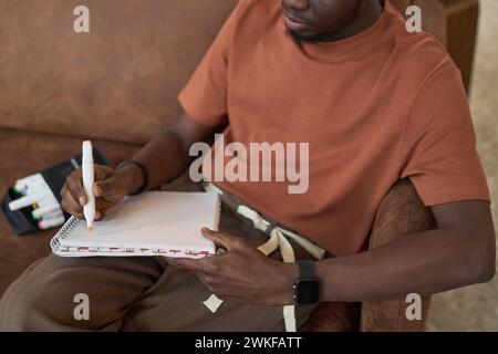 Close up of unrecognizable Black young man sketching with color markers sitting on couch Stock Photo