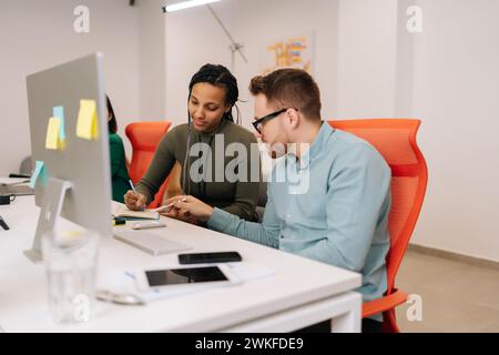 Two focused young diverse business people analysts partners talking, working together, discussing data management using desktop computer. Stock Photo