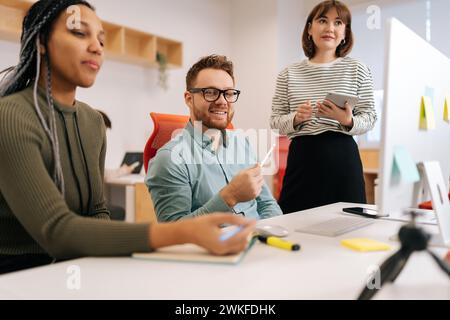 Happy multiethnic colleagues employees cooperating in office talking working together at workplace. Diverse young startup business team coworkers Stock Photo