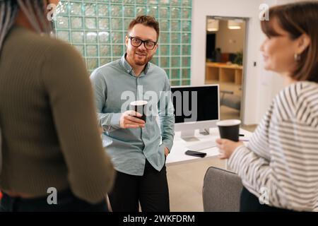 Happy group of ethnically diverse young man and women relaxing while having coffee break at work in light modern office room. Relaxed coworkers Stock Photo