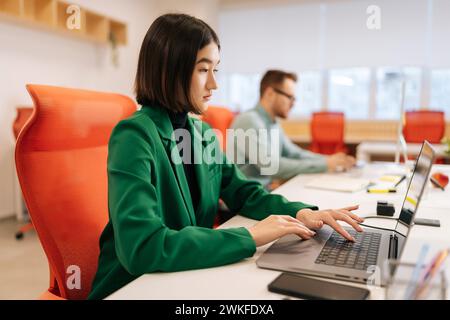 Young successful startup team working on laptop sitting together at coworking workplace. Focused business people businessmen and businesswoman typing Stock Photo