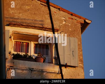 Antique stone house in the old town. Window under the roof. Colored thread curtains and a flower on the windowsill. Rovinj, Croatia - February 13, 202 Stock Photo