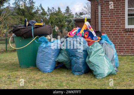 Pile of bulky waste in front of a house with garbage bags, rain barrels and toys Stock Photo
