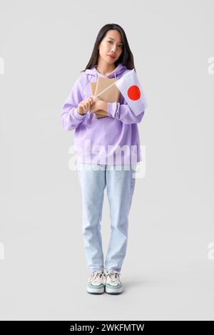 Female Asian student with books and flag of Japan on light background Stock Photo