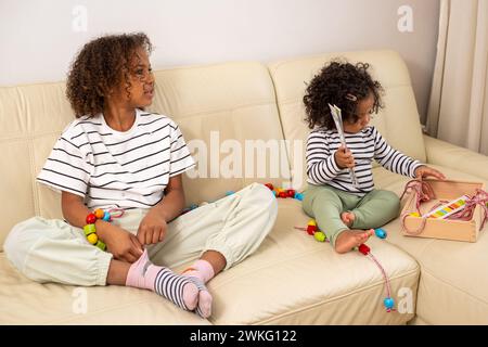 Two mixed race girls are sitting on a couch and playing with toys, symbolizing eco friendly toy, occupation and learning Stock Photo