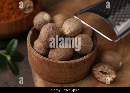 Nutmegs in bowl and grater on table, closeup Stock Photo