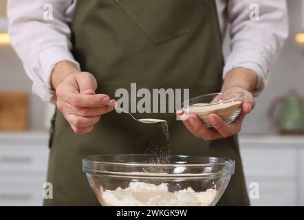 Making bread. Man putting dry yeast into bowl with flour in kitchen, closeup Stock Photo