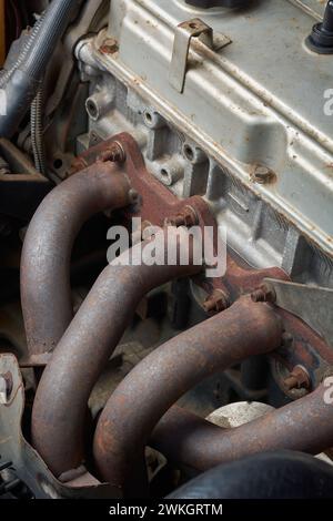 used exhaust manifold of four cylinder car engine, component of internal combustion engine collects exhaust gases made of cast iron and bolted Stock Photo