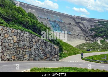 View from road pass road alpine road to road level below in front of outside of large dam wall of reservoir Lac du Mont Cenis Mont-Cenis reservoir Stock Photo