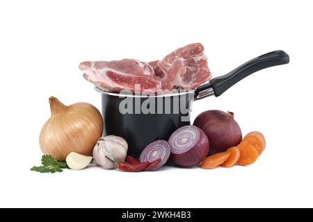 Black saucepan with pieces of raw pork inside. Around the saucepan are sliced vegetables which include onions, carrots, and garlic isolated on white b Stock Photo