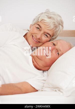 Senior couple, portrait and together in bed, relaxing and love in retirement for bonding on weekend. Elderly people, bedroom and resting or happy in Stock Photo