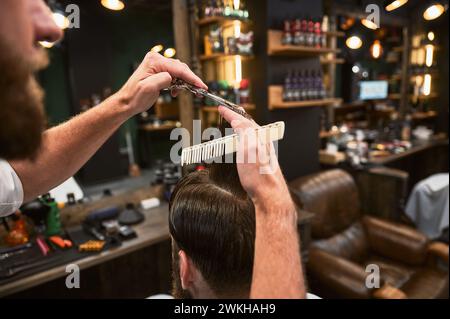 Close-up photo of barber cutting wet hair. Professional hairdresser making fresh hairstyle. Back view of man getting new haircut. Stock Photo