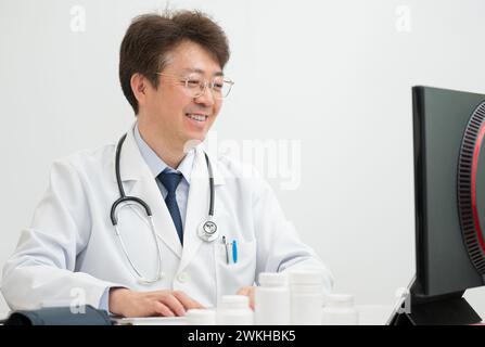 A middle-aged male doctor performing telemedicine using a computer Stock Photo