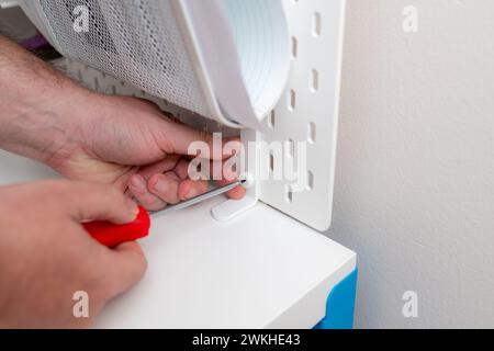 Man screws pegboard on white work table with screwdriver Stock Photo