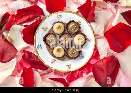 Elegant artisan chocolates decorated with hazelnuts, caramel crumbs and golden pearls arranged on vintage plate with floral design on background of co Stock Photo