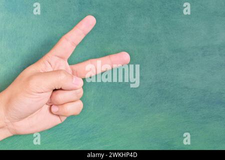 Young male Asian hand making peace sign or letter v sign isolated on green background. Stock Photo