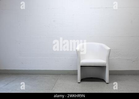 Old vintage, well-used white leather armchair set against grungy concrete wall, no people. Stock Photo