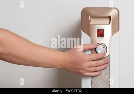 A man's hand regulates the heating power of an electric air heater in an apartment, close-up. Copy space for text Stock Photo