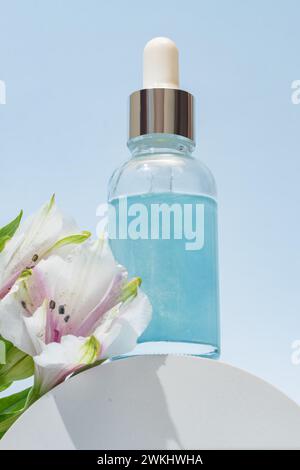 Aestethic image with abstract cosmetic product, serum, oil y etc. Glass dropper bottle with pipette and label on white podium with alstromeria flowers Stock Photo