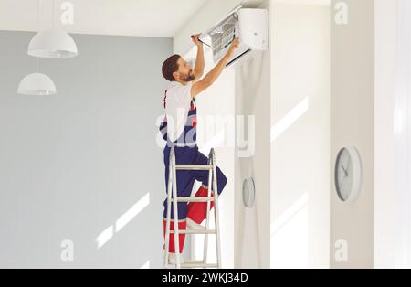 Male professional worker repairs air conditioner and cleans filters in client's apartment. Stock Photo