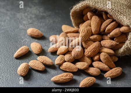 Delicious sweet almonds in wooden bowl or burlap sack on rustic background, roasted almond nut, healthy food Stock Photo