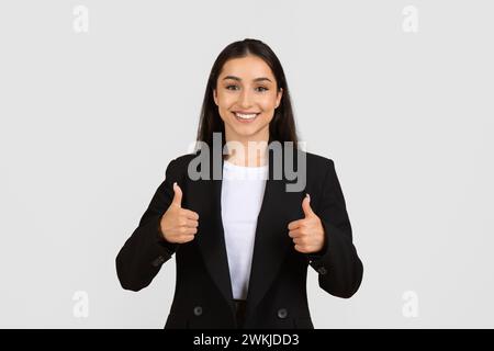 Smiling businesswoman giving thumbs up in black suit Stock Photo