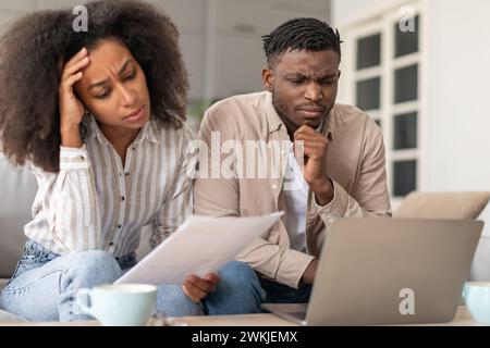 Frowning African American married couple using laptop doing paperwork indoor Stock Photo