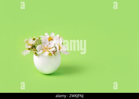 One white egg in a stand with spring pear and strawberry flowers on a green background. Happy Easter Stock Photo