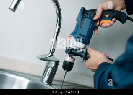 closeup of a man, wearing blue overalls, drilling a hole in a metal sink with a drill Stock Photo