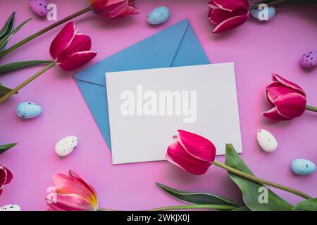 White empty envelope copy space Easter eggs with pink tulips on violet pastel background. Greeting card Postcard. Flat lay composition top view. Decoration minimalist modern design template. Floral layout Concept of creative spring holiday mock up.  Stock Photo