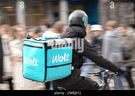 Belgrade, Serbia - February 20, 2024:  Wolt service courier with a delivery bag riding bike in busy city street full of pedestrians, rear view Stock Photo