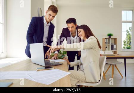 Company employees talking with colleagues on workplace in office looking at laptop monitor screen. Stock Photo