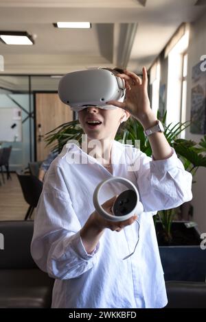 Young woman in professional attire testing new VR equipment in modern office, exploring virtual reality for business use. Stock Photo