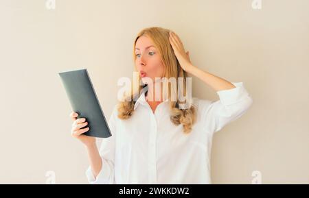 shocked and surprised caucasian young woman employee looking at digital tablet computer or folder with documents, emotional overworked office manager Stock Photo