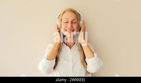 Portrait of happy relaxed middle aged woman listening to music in wireless headphones on white background Stock Photo