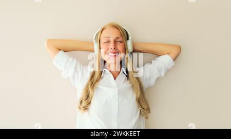 Portrait of happy relaxed middle aged woman listening to music in wireless headphones on white background Stock Photo