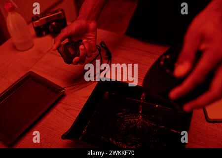 focus on timer in hand of photographer pours developer into tray for film processing, red darkroom Stock Photo