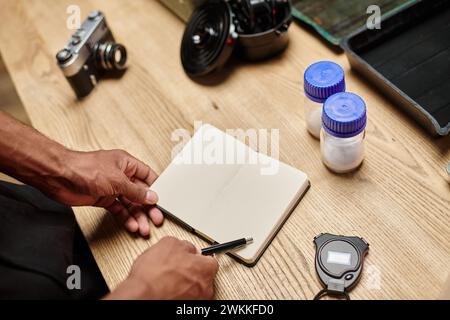 cropped african american man holding pen near notebook and bottles with film developing powder Stock Photo
