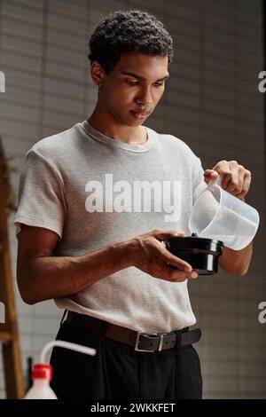 focused african american photographer pouring chemical solution into film developing tank Stock Photo