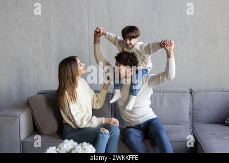 Cheerful family having fun and playing with little son while chilling together on sofa in living room Stock Photo