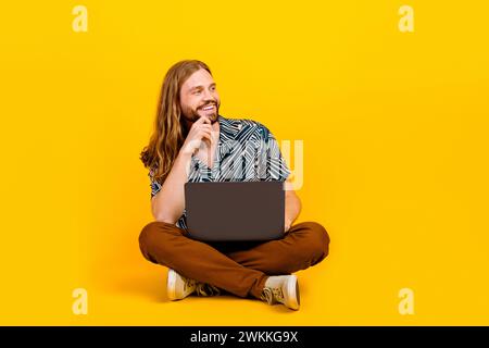 Full length photo of funky dreamy guy wear print shirt working modern device looking empty space isolated yellow color background Stock Photo