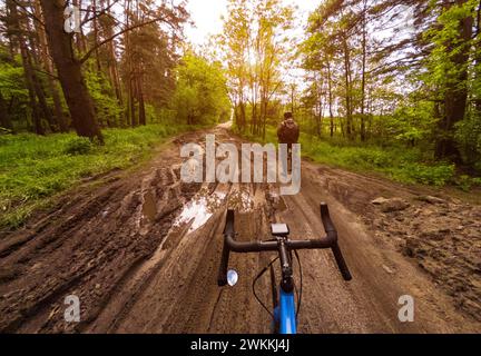 Two cyclists on gravel bicycles in a beautiful forest on a dirt road with puddles. Cyclists have a rest during training. First person view. Stock Photo